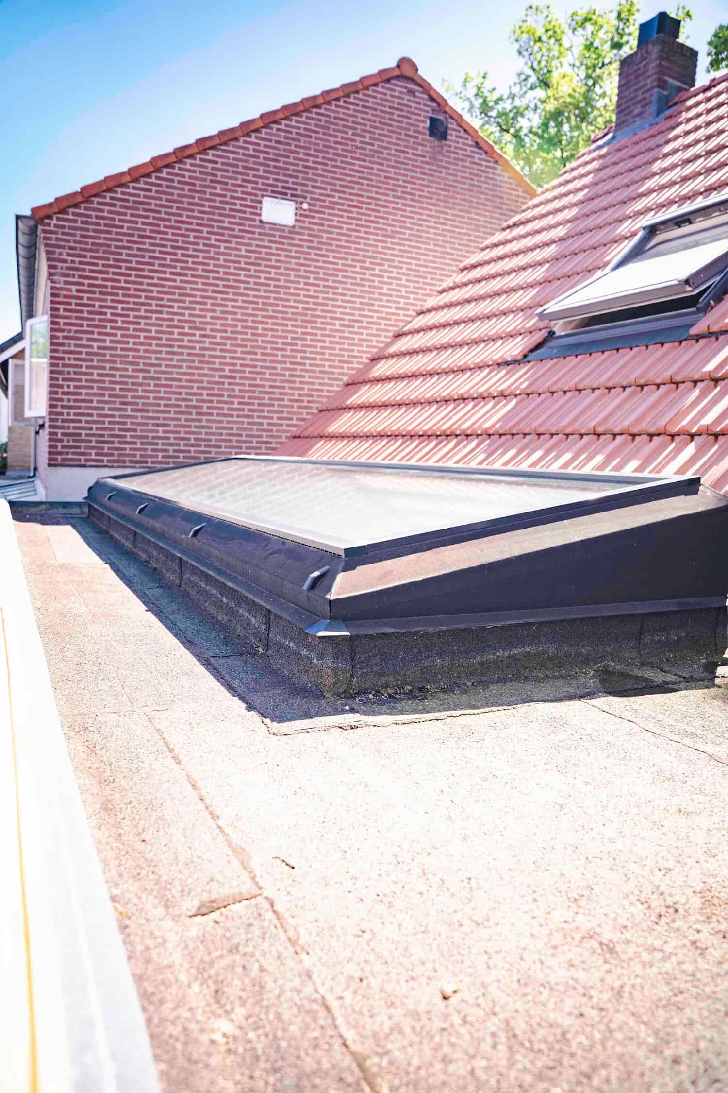 Lichtstraat op een plat dak met daarachter het pannendak en de schoorsteen